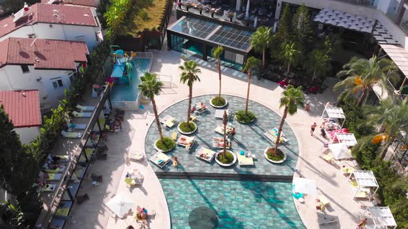 Fly Over a Large Pool with Blue Water and a Lot of Tourists in Hot Weather