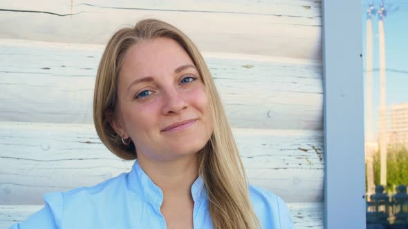 A Beautiful Young Blonde Woman with Blue Eyes Looks Into the Frame and Smiles with a Natural Smile