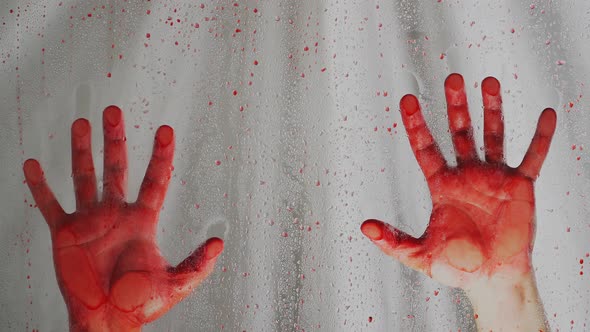 Bloody hands on a white background. Behind a transparent glass covered with red drops. Close up