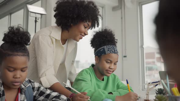 African American female teacher standing with pupils teaching writing lesson in modern classroom.