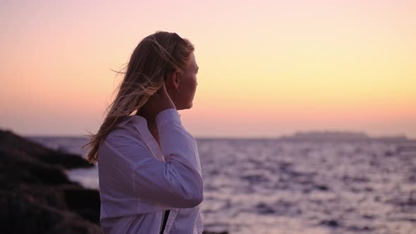 Attractive Young Woman at Sunset on Background of Ocean or Sea in White Shirt and Black Top Looks