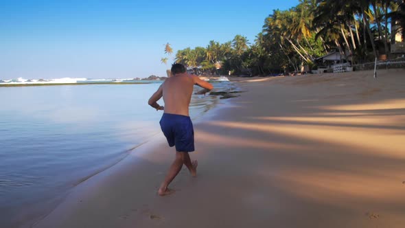 Handsome Athlete Runs Doing Exercises Along Ocean Coast