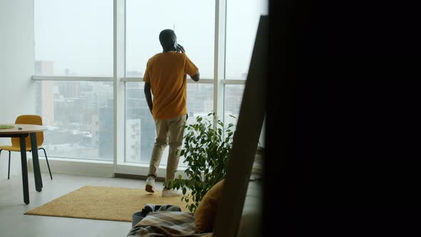 African American Man Speaking on Mobile Phone Walking at Home Looking Out of Panoramic Window