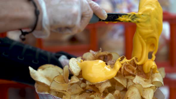 Closeup of someone putting cheese sauce onto a serving of curly fries.