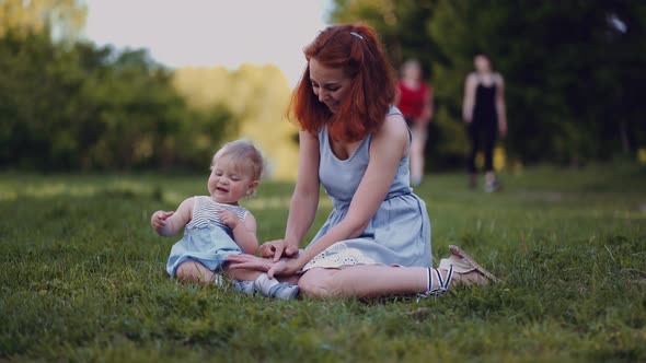 mother and baby sit in a park or in a forest on the ground looking at twigs and cones