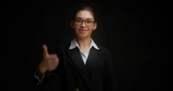 Asian Woman in Business Clothes and Glasses Smiles and Gives a Thumbs Up