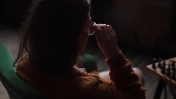 Back View of Intelligent Young Woman Putting on Glasses and Making Move in Chess Game Sitting at