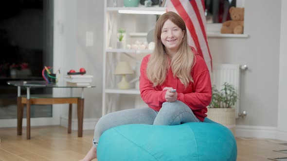 Wide Shot of Cheerful Asian Girl Switching Channels with Remote Control and Laughing