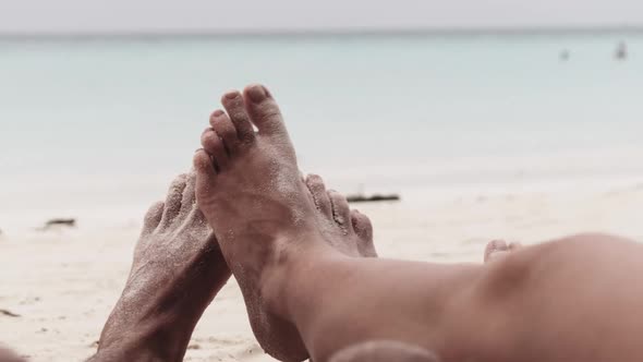 POV Feet of a Couple of Men and Women Lying on a Tropical Sandy Beach By Ocean