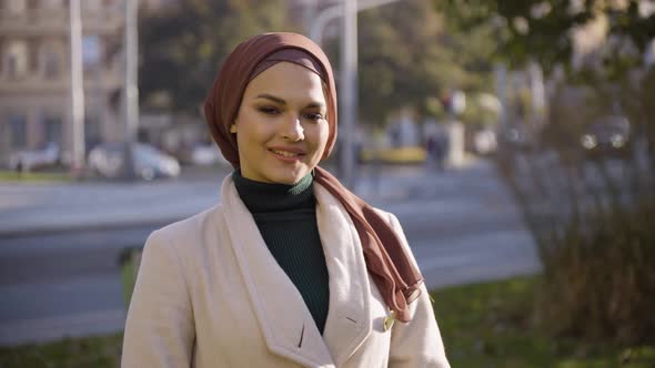 A Young Beautiful Muslim Woman Waves at the Camera with a Smile in a Park in an Urban Area  Closeup