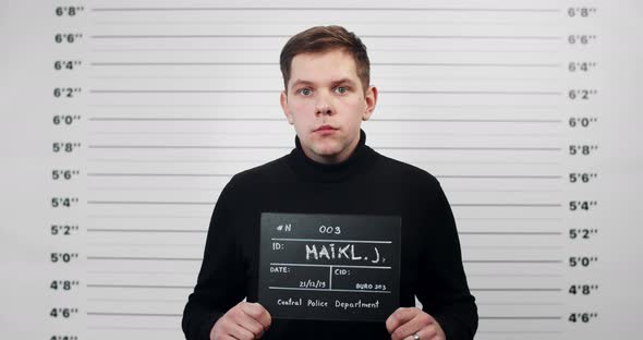 Portrait of Guy in Black Turtleneck Holding Sign for Photo in Police Department