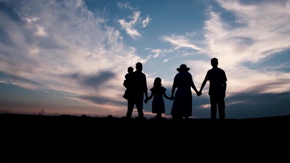 Silhouettes of Happy Family Holding the Hands in the Meadow During Sunset