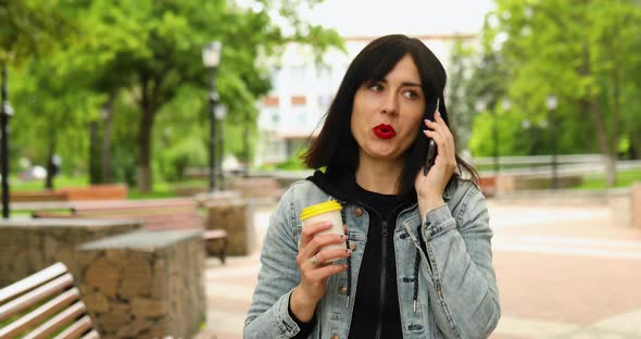 Brunette woman holding take away coffee and talking by phone