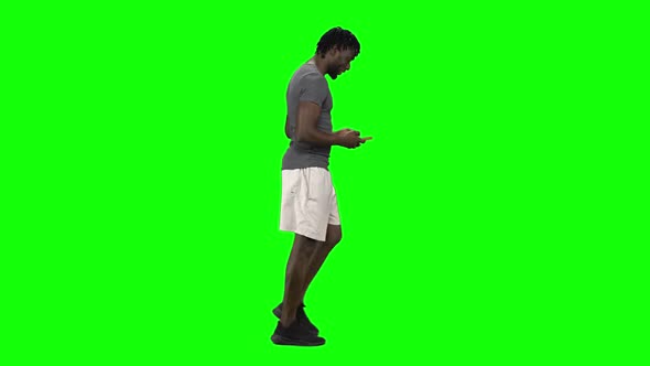 African American Man Walking and Texting Message Vie Mobile Phone at Green Screen, Chroma Key