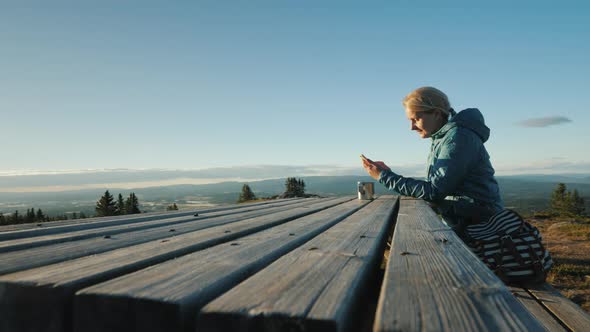 A Woman Sits at a Table Uses Her Phone High in the Mountains of Norway
