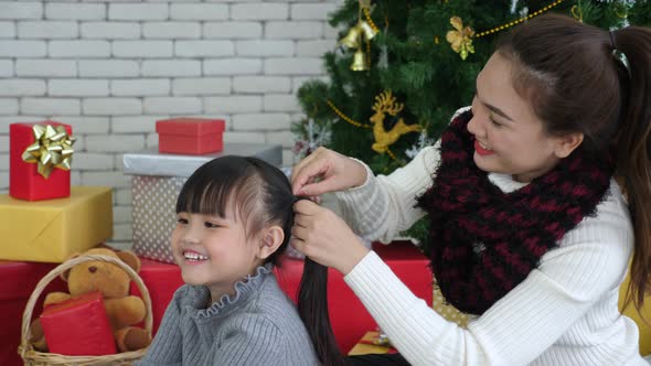 Asian mother in sweater making pigtails to daughter in pajamas in Christmas