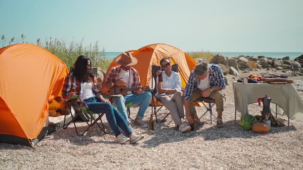 Four Friends on Picnic Drinking Cold Beer and Clinking Bottles at Hot Sunny Day on Beach