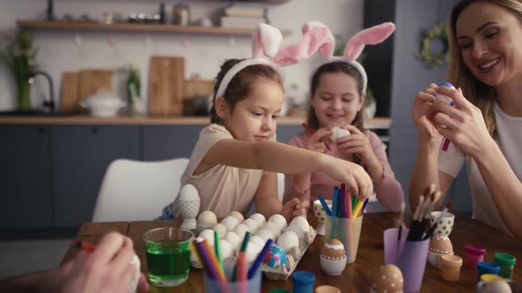 Zoom out of caucasian family of four people chatting and decorating easter eggs in domestic kitchen.