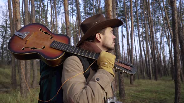 A Backpacker in a Hat with a Guitar in the Forest