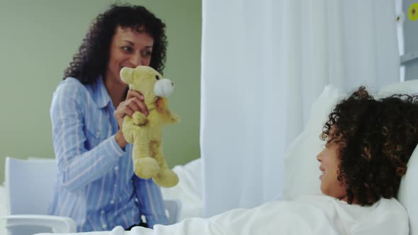 Front view of African american mother giving teddy bear to her son in the ward at hospital 