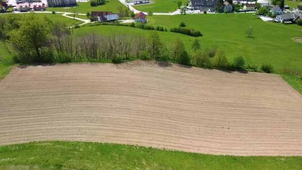 Flying over small ploughed dry field prepared to be seeded with corn. Aerial 4k view.