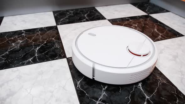 The Robot Vacuum Cleaner Cleans in the Modern House on the Tiles Floor at Kitchen