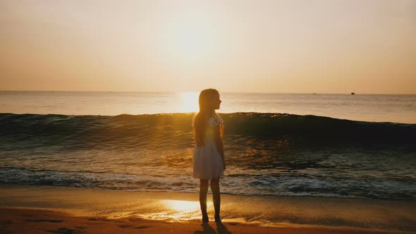 Cinematic Back View Shot of Happy Little Girl Watching Sea Wave Coming on at Incredible Golden Ocean