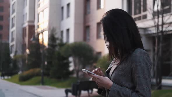 Portrait of a Confident Business Woman in a Suit Uses a Smartphone Outdoors