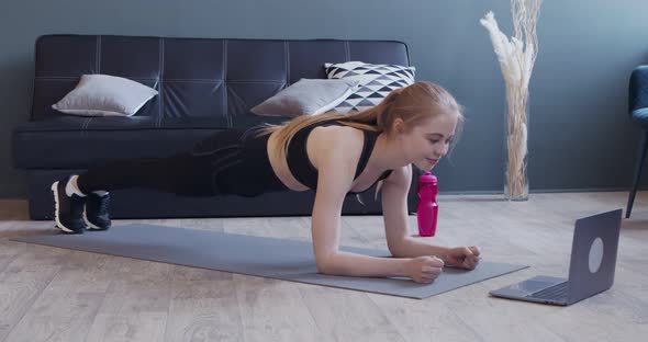 Young Fit Girl Standing in Plank Watching Tutorial on Laptop