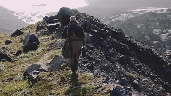 Man In Greatcoat Walking Along Rocky Ridge Towards Sunlit Valley