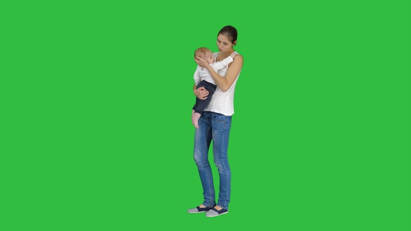 Young Mother Trying to Calm Down Infant Son on A Green