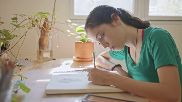 Teenage artist sitting drawing in a sketchbook in her room