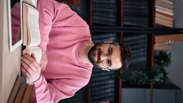 VERTICAL VIDEO POV Smiling Latino Modern Bearded Man Reading Book at Library Posing Desk Workplace