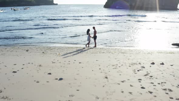 Man and Woman Walking Along Tropical Beach at Sunset, Tracking Aerial Shot of Young Couple