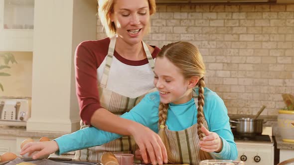 Smiling mother and daughter wearing apron arranging unbaked cookies 4K 4k