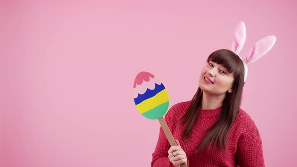 Caucasian Woman Covering Her Face with Colorful Cardboard Easter Egg While Wearing Bunny Ears