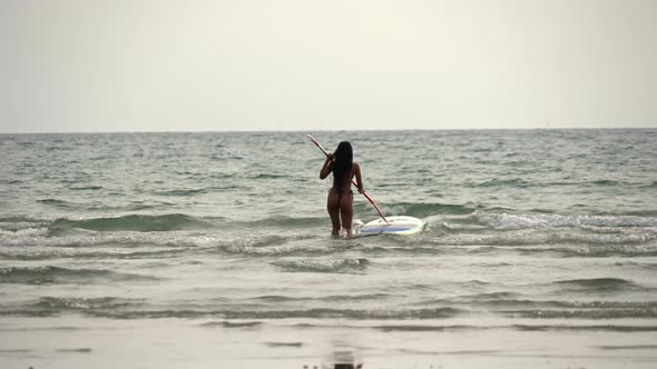 Woman Pushing Paddleboard Out To Sea