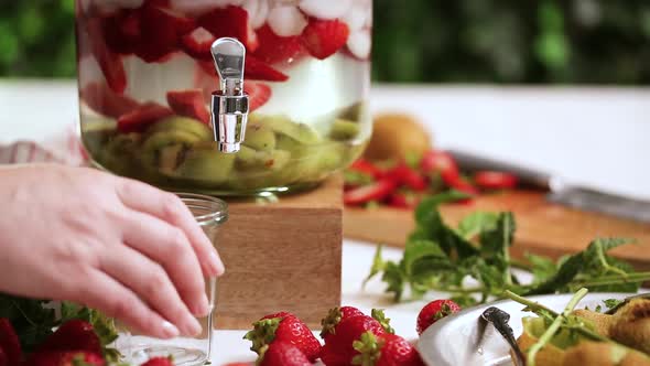 Pouring infused water with organic strawberries, kiwi and fresh mint from glass beverage drink dispe