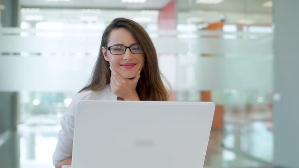The Girl in a Spacious Bright Office, at a Desk With a Laptop. He Looks at the Camera and Smiles