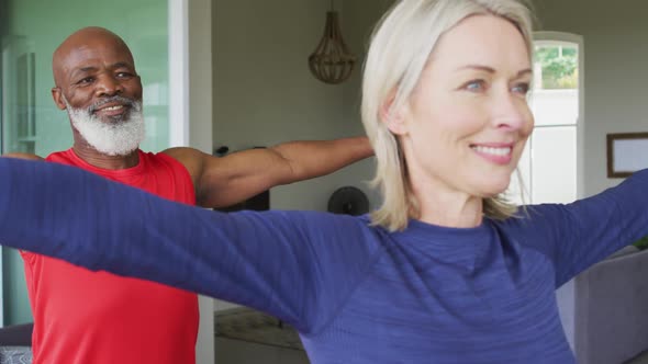 Mixed race senior couple performing stretching exercise together at home