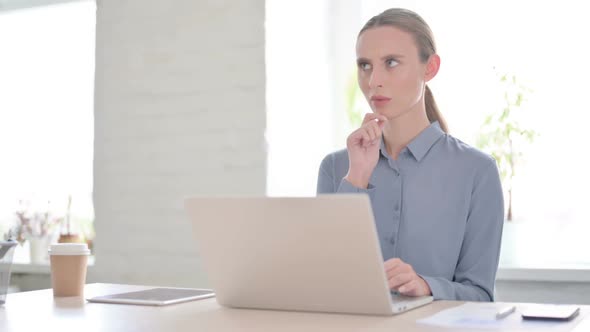 Woman Thinking While Working on Laptop in Office