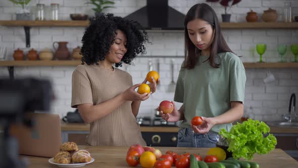 Cheerful African American and Korean Women Talking Smiling Standing in Kitchen Indoors