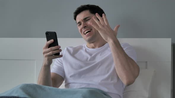 Young Man Reacting To Loss, Using Smartphone in Bed
