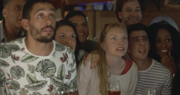 Sports enthusiasts celebrating victory while watching televised match in bar, slow motion