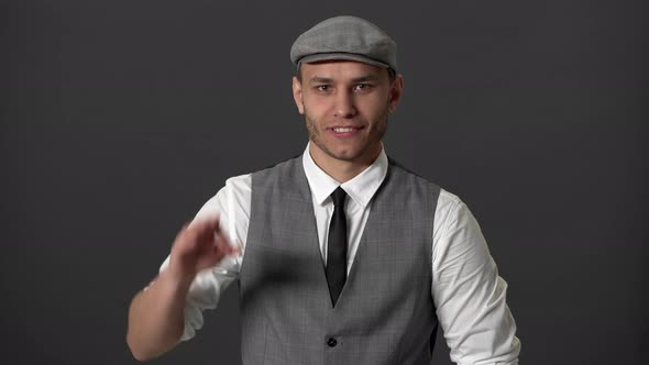 Portrait of Content Gentleman in Vintage Suit and Flat Cap Gesturing Ok Sign Over Grey Background