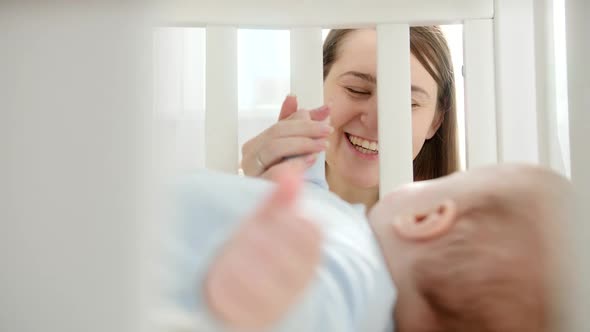 Portrait of Happy Laughing Woman Looking and Holding Her Baby Lying in Crib