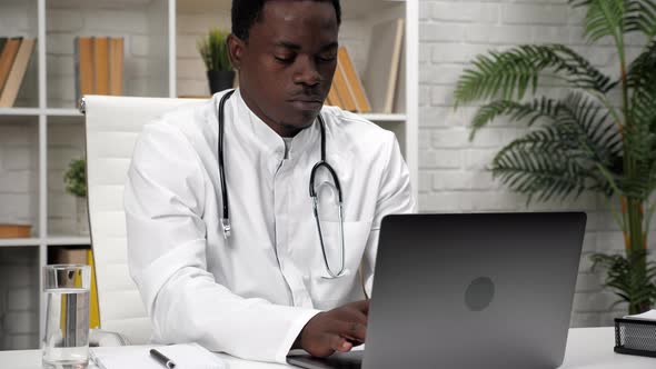 African American Man Doctor Typing Text on Keyboard Laptop in Clinic Office