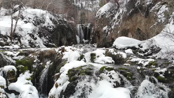 Flying up towards waterfall with snow in winter in 4K