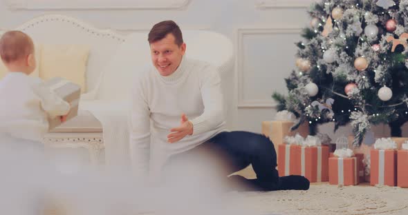 Little Son Carries Dad Boxes with New Year's Gifts Under the Christmas Tree