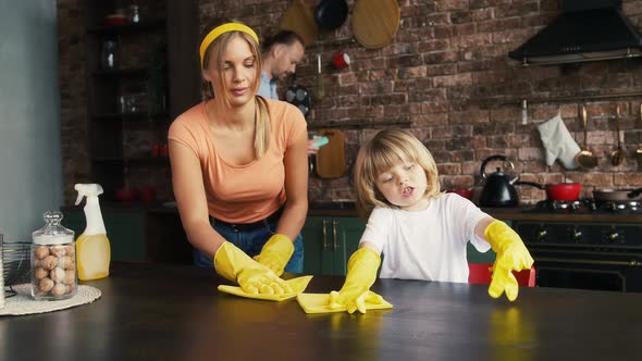 Mom and Her Kid in Yellow Rubber Gloves are Smiling and Talking Cleaning Table By Rags Using